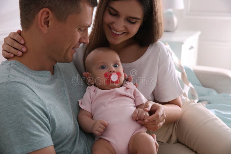 Happy couple holding their cute little baby with pacifier at home royalty free stock photography