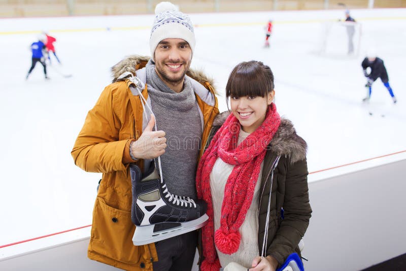 People, friendship, sport and leisure concept - happy couple with ice-skates on skating rink