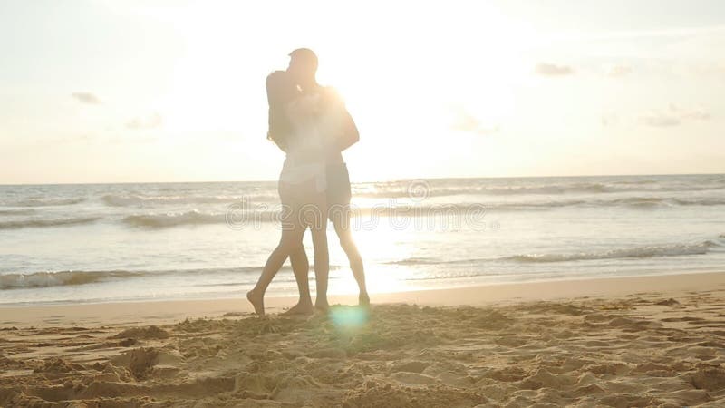 Happy couple kissing and hugging each other at the sea beach at sunset. Young man and woman in love having fun together