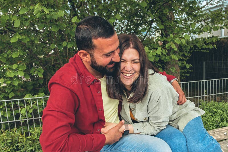 Happy couple laughs as boyfriend tickles girlfriend on park bench. Joyful moment of affection, bonding, and carefree royalty free stock image