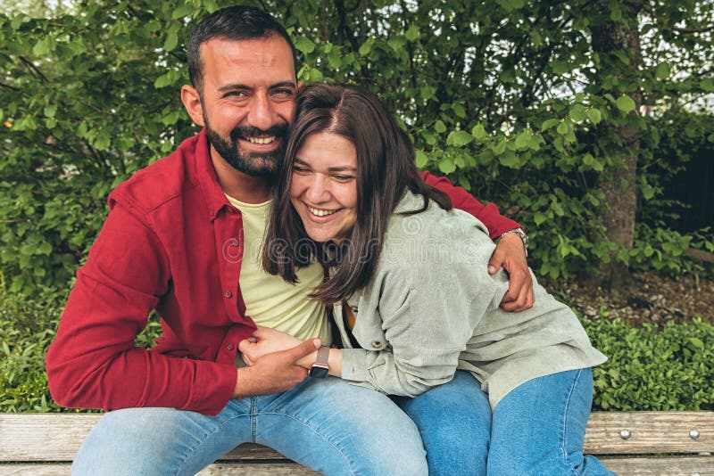 Happy couple laughs as boyfriend tickles girlfriend on park bench. Joyful moment of affection, bonding, and carefree royalty free stock image