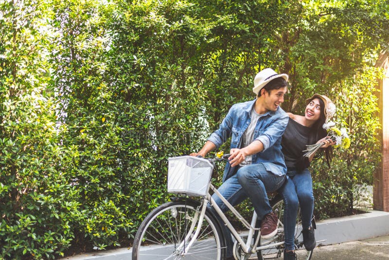 Happy couple riding bicycle together in romantic view park background. Valentine`s day and wedding honeymoon concept. People and