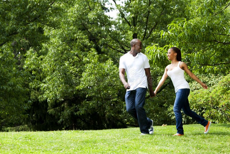 Krásná zábava spokojený úsměv afroamerické mladý pár běží, hraje v parku, na sobě bílé košile a modré džíny.