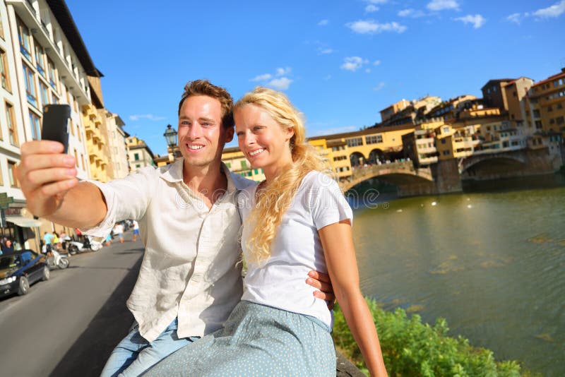 Happy couple selfie photo on travel in Florence. Romantic women and men in love smiling happy taking self portrait outdoor by Ponte Vecchio during vacation holidays in Florence, Tuscany, Italy, Europe