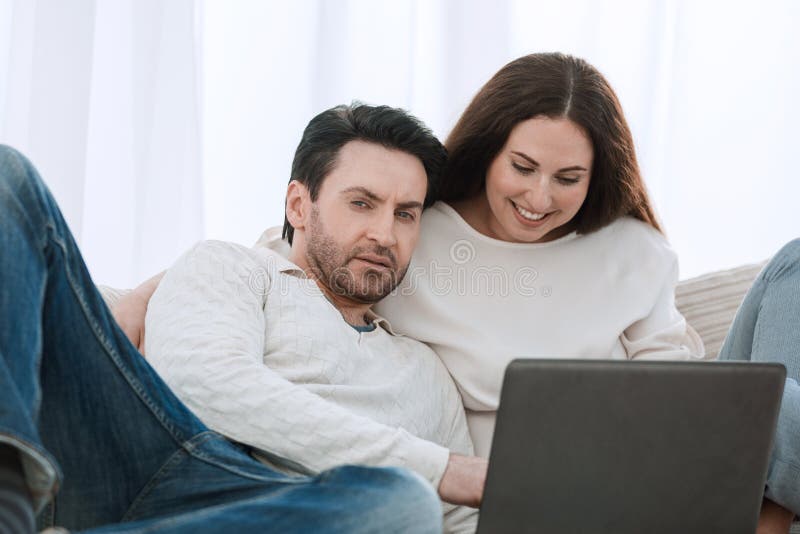Happy couple sitting on the couch in her arms, looking at laptop royalty free stock photo Happy couple sitting on the couch in her arms, looking at laptop royalty free stock photo