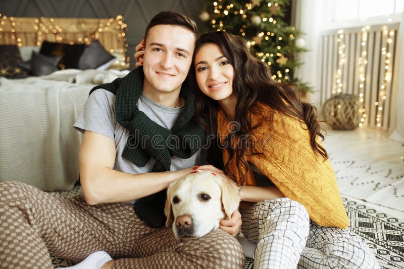 Happy couple is sitting near the bed with a dog, christmas. new year at home. family and date royalty free stock photography Happy couple is sitting near the bed with a dog, christmas. new year at home. family and date royalty free stock photography