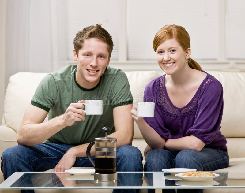 Happy couple sitting on sofa drinking fresh coffee royalty free stock photography