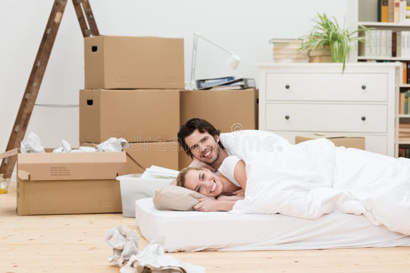 Happy couple sleeping on the floor in their new home lying on a mattress in the living room surrounded by cardboard boxes. Happy couple sleeping on the floor in their new home lying on a mattress in the living room surrounded by cardboard boxes