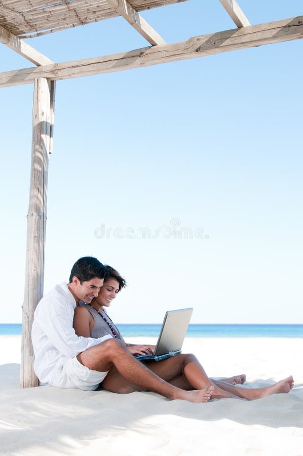 Beautiful young couple surfing the net together during summer vacation at tropical beach. Beautiful young couple surfing the net together during summer vacation at tropical beach