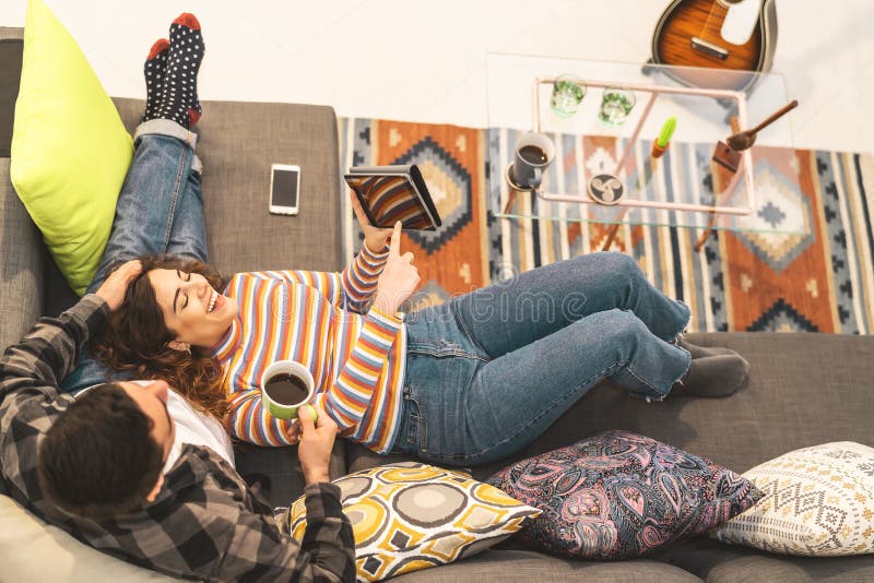 Happy couple using tablet while relaxing on sofa at home - Young romantic lovers having fun with new trends technology devices stock images Happy couple using tablet while relaxing on sofa at home - Young romantic lovers having fun with new trends technology devices stock images