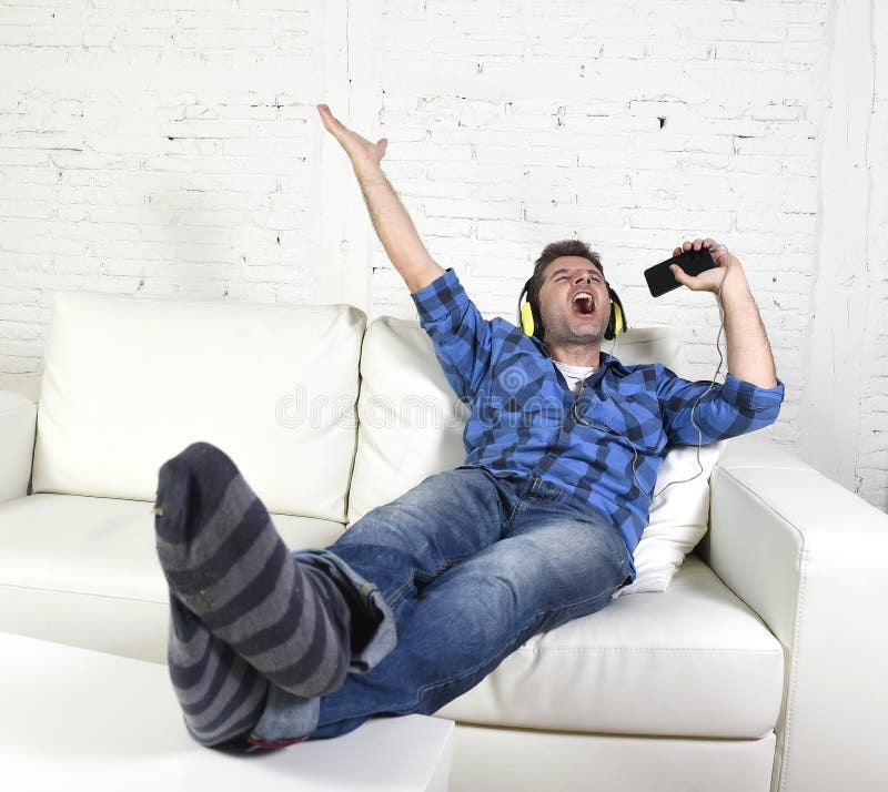 Happy crazy man on couch listening to music holding mobile phone as microphone stock photography Happy crazy man on couch listening to music holding mobile phone as microphone stock photography