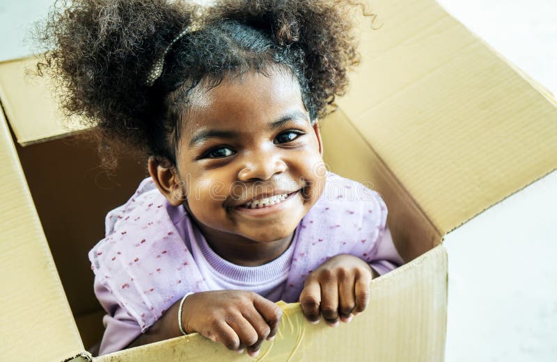 Happy cute active little african american kids girl play riding in cardboard boxes feel excited to move in new house, playful overjoyed black sister have fun
