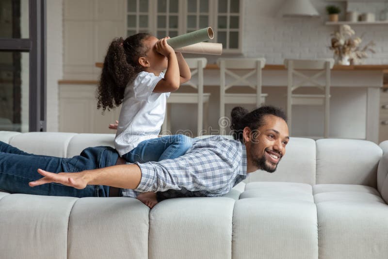 Happy cute African American daughter girl riding cheerful dads back royalty free stock image