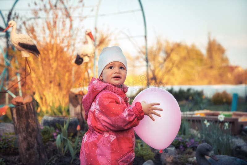 Happy cute baby girl playing with balloon outdoors on backyard in countryside stock photo