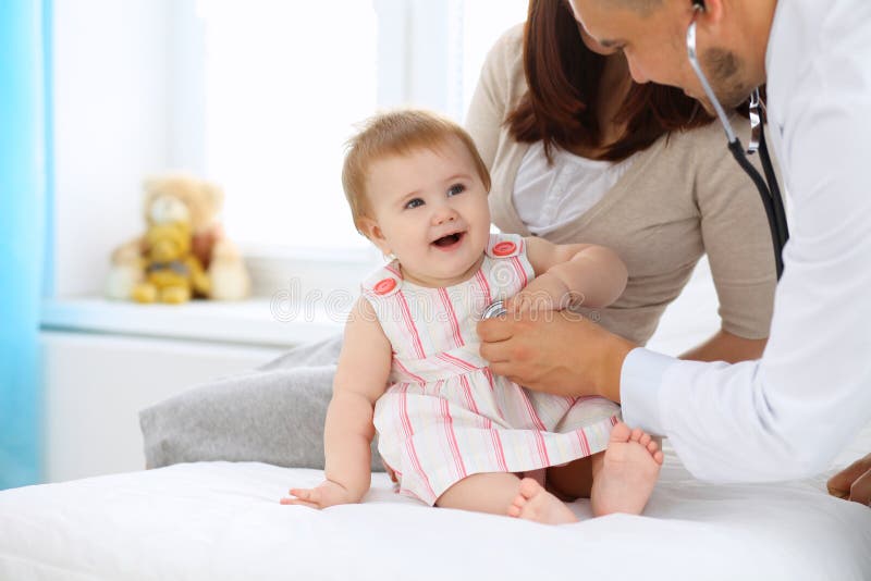 Happy cute baby with her mother at health exam at doctor`s office. Intern, nurse.