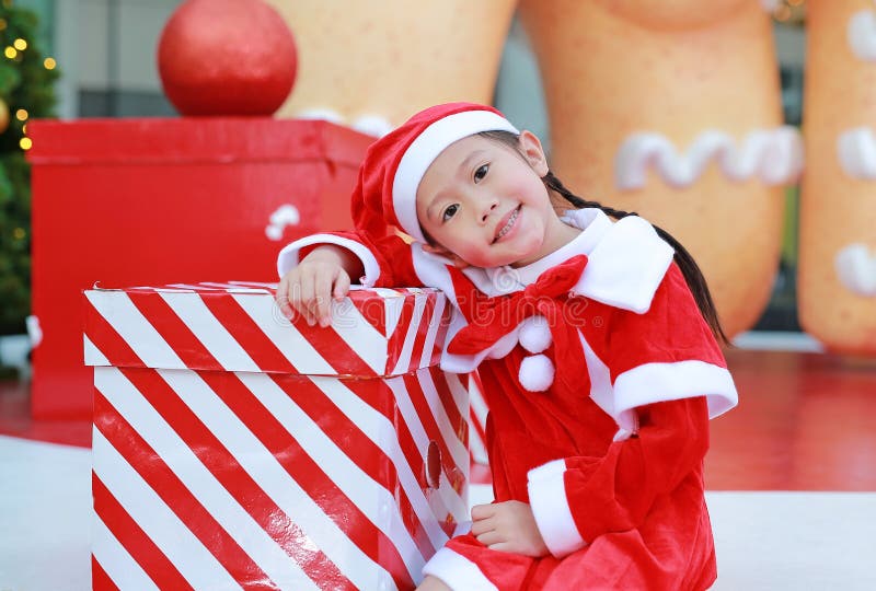 Happy cute little Asian child girl in santa costume with gift box near christmas tree and background. Christmas winter holiday con stock photo Happy cute little Asian child girl in santa costume with gift box near christmas tree and background. Christmas winter holiday con stock photo
