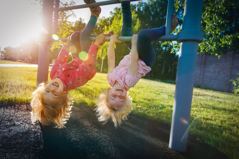 Happy cute little girls upside down on monkey bars at sunset. 