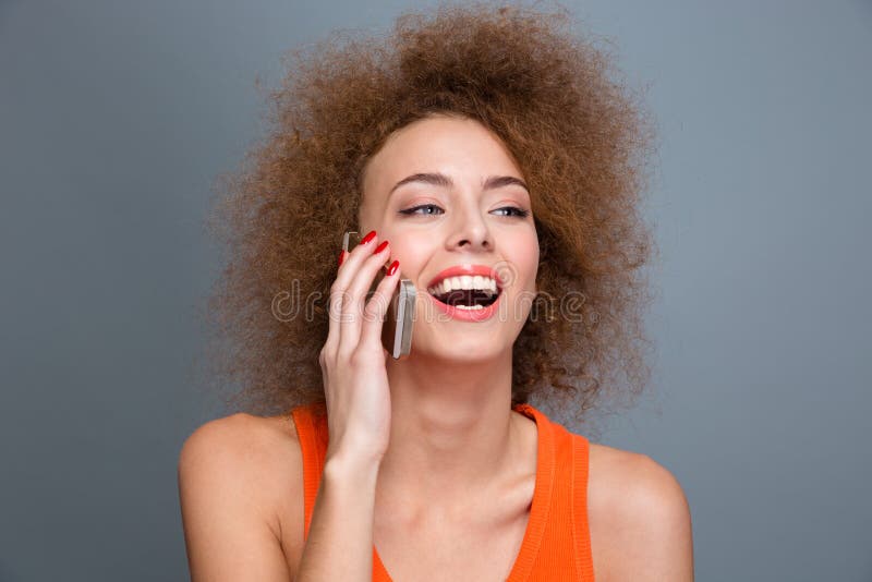 Happy delightful curly woman talking on mobile phone and laughing