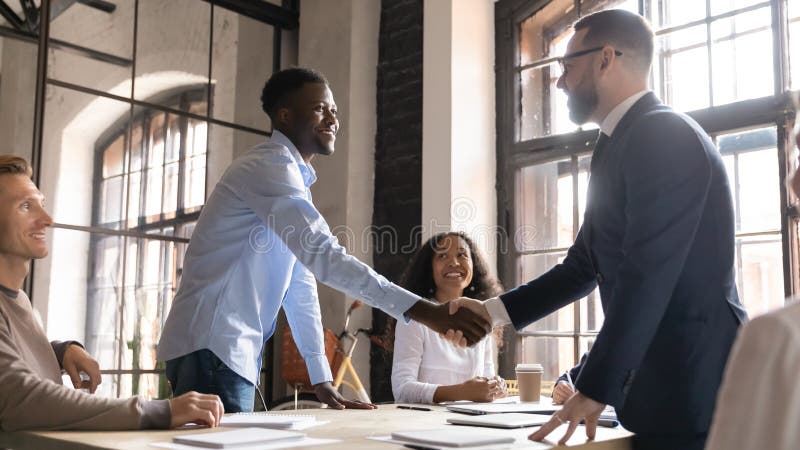Happy diverse business partners handshaking at group negotiation. Happy diverse business partners handshaking at successful group negotiation, making agreement