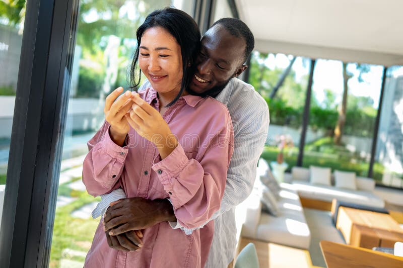 Happy and diverse couple sharing a joyful moment at home, embracing and smiling together stock image