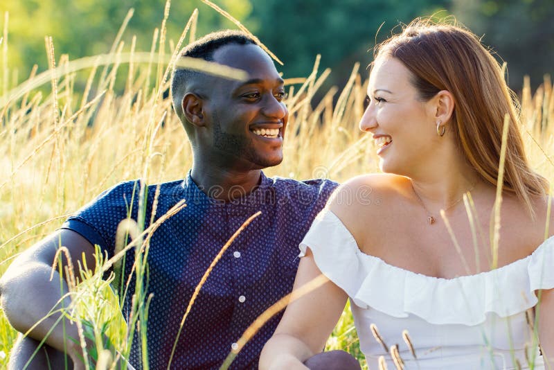 Happy diverse couple sitting in grass field.