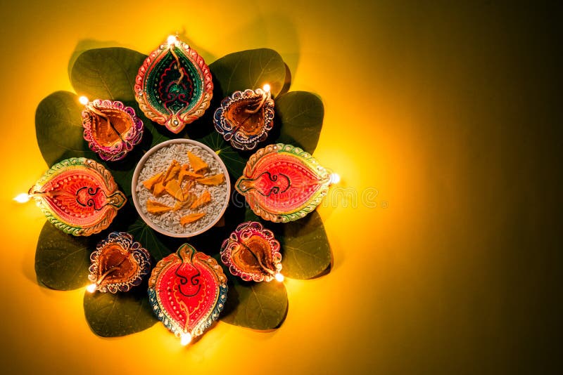 Happy Dussehra. Clay Diya lamps lit during Dussehra with yellow flowers, green leaf and rice on yellow pastel background. Dussehra