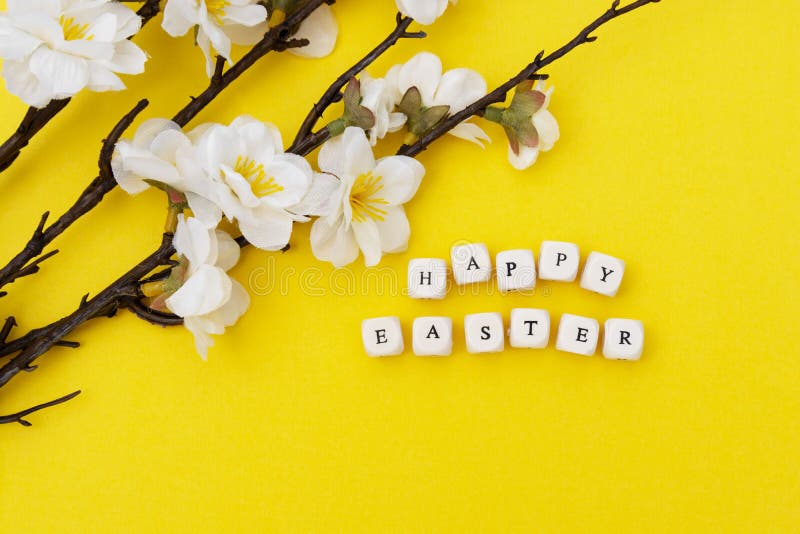 Happy Easter. Cubes with text on yellow background. Spring brunches with white flowers. Minimalistic flat lay stock photography Happy Easter. Cubes with text on yellow background. Spring brunches with white flowers. Minimalistic flat lay stock photography