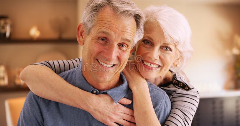 Happy elderly couple sitting at home smiling at camera stock image