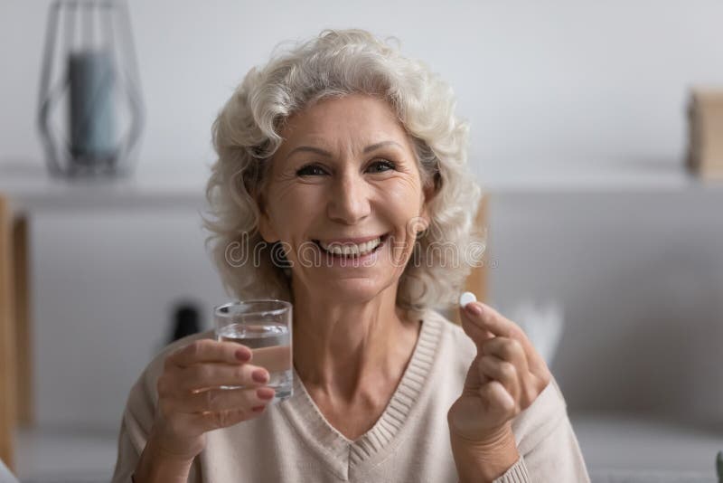 Happy elderly senior woman holding glass of water and pill.