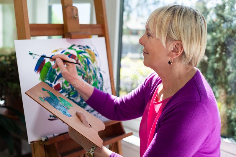 Happy elderly woman painting for fun at home