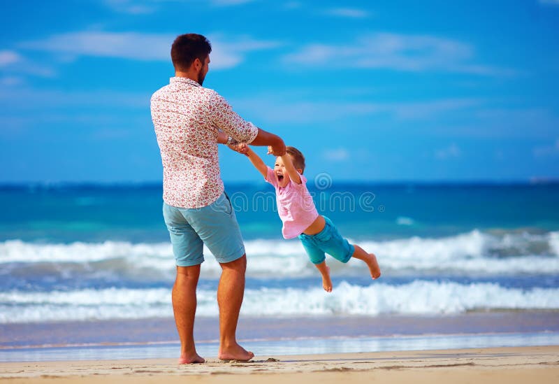 Happy excited father and son playing on summer beach, enjoy life