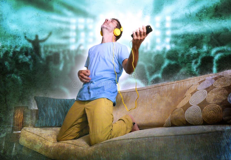 Happy and excited man jumping on sofa couch listening to music with mobile phone and headphones playing air guitar crazy imagine stock images Happy and excited man jumping on sofa couch listening to music with mobile phone and headphones playing air guitar crazy imagine stock images