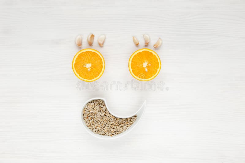 Happy face of fruit and seeds. The smiling face is made from oranges, garlic and sunflower seeds. Background of useful antiviral