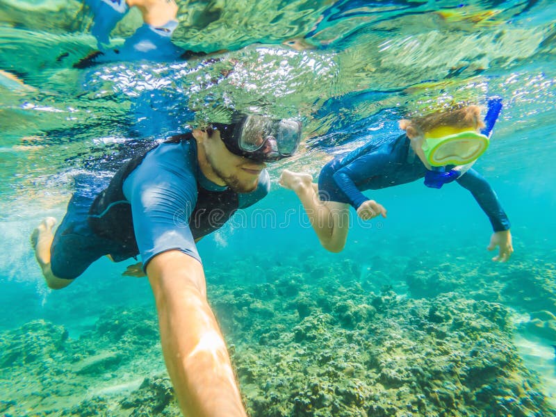 Happy family - active kid in snorkeling mask dive underwater, see tropical fish in coral reef sea pool. Travel adventure