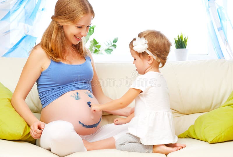 Happy family in anticipation of the baby. Pregnant mother and child daughter paint colors on the tummy. Happy family in anticipation of the baby. Pregnant mother and child daughter paint colors on the tummy