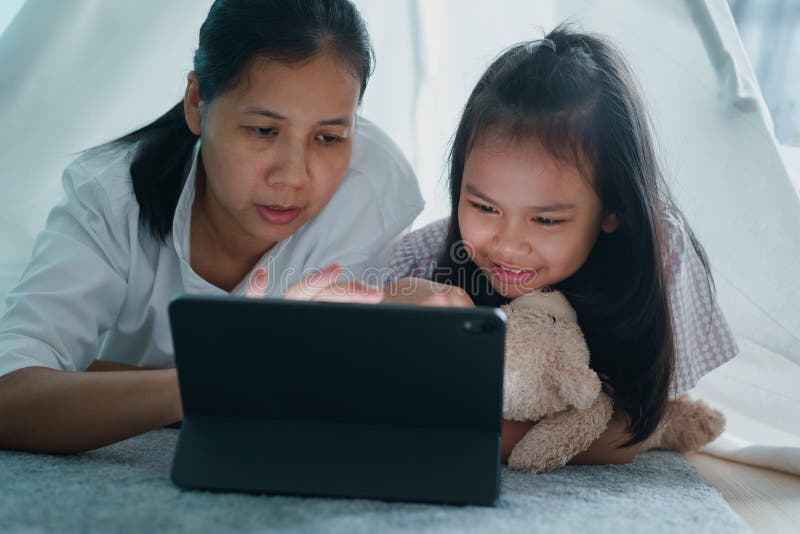 Happy family of Asian mother and daughter using tablet in a tent at night. Asia children hug a doll, talk, and learning on the. Digital computer at home stock images Happy family of Asian mother and daughter using tablet in a tent at night. Asia children hug a doll, talk, and learning on the. Digital computer at home stock images