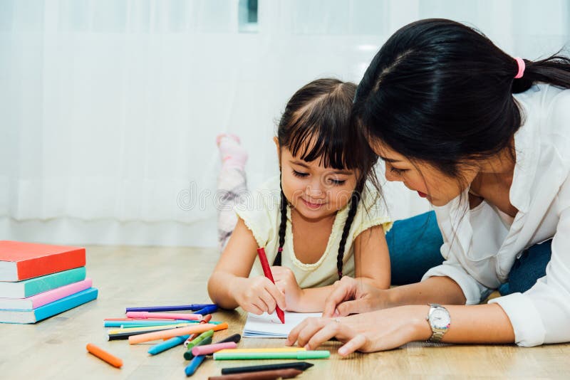 Happy Asian child kid daughter kindergarten and young beautiful parent mother teaching drawing and play color together at interior room home, family day and Back to school concept. Happy Asian child kid daughter kindergarten and young beautiful parent mother teaching drawing and play color together at interior room home, family day and Back to school concept