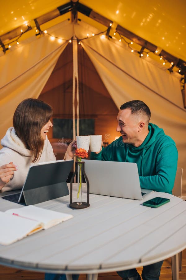 Happy family couple freelancers working laptop on a cozy glamping tent in summer evening. Luxury camping tent for outdoor holiday
