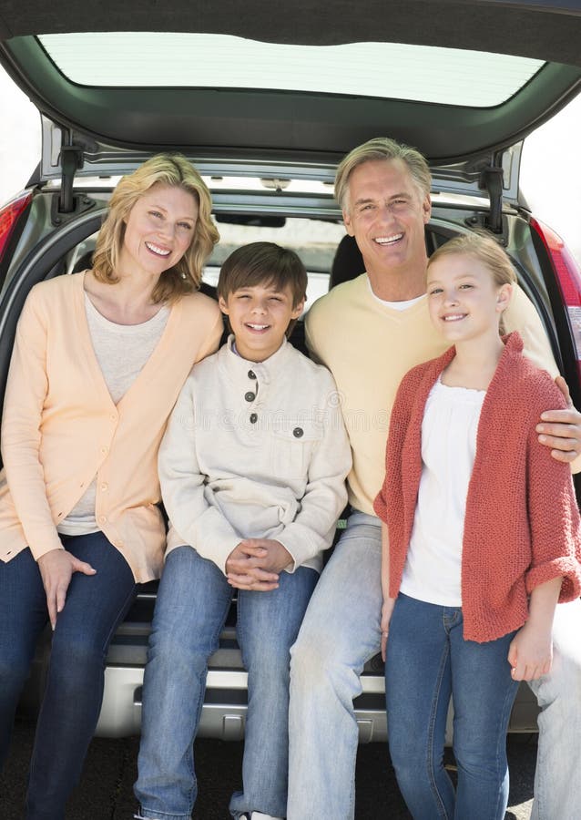 Happy Family Of Four Sitting In Car Trunk
