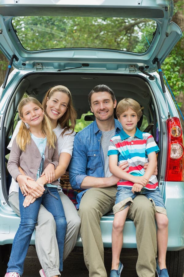 Happy family of four sitting in car trunk