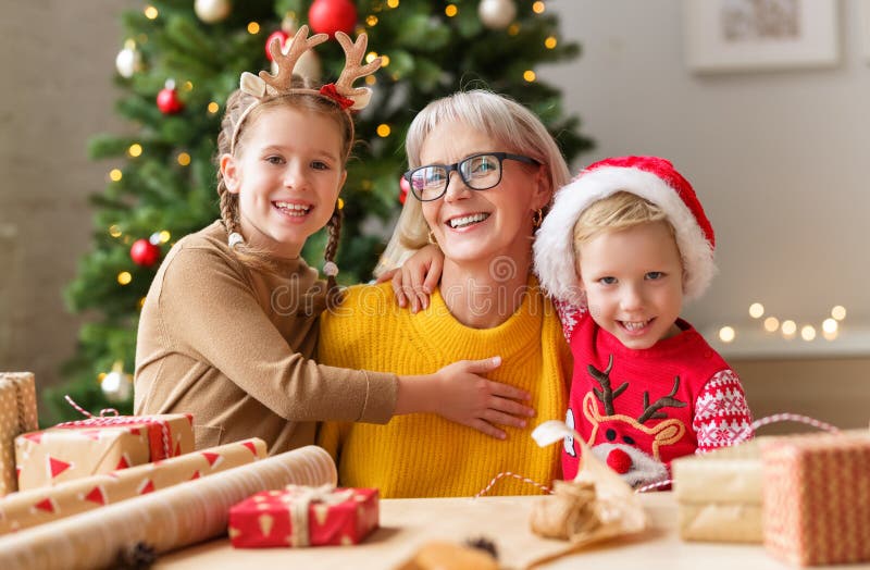 Happy family grandma and grandkids hug and smile for camera while wrapping Christmas gifts near a beautiful Christmas tree. Happy family grandmother and royalty free stock photo
