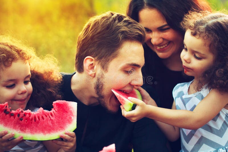 Happy family having a picnic in the green garden. Smiling and laughing people eating watermelon. Health food concept. Twin sisters stock images Happy family having a picnic in the green garden. Smiling and laughing people eating watermelon. Health food concept. Twin sisters stock images