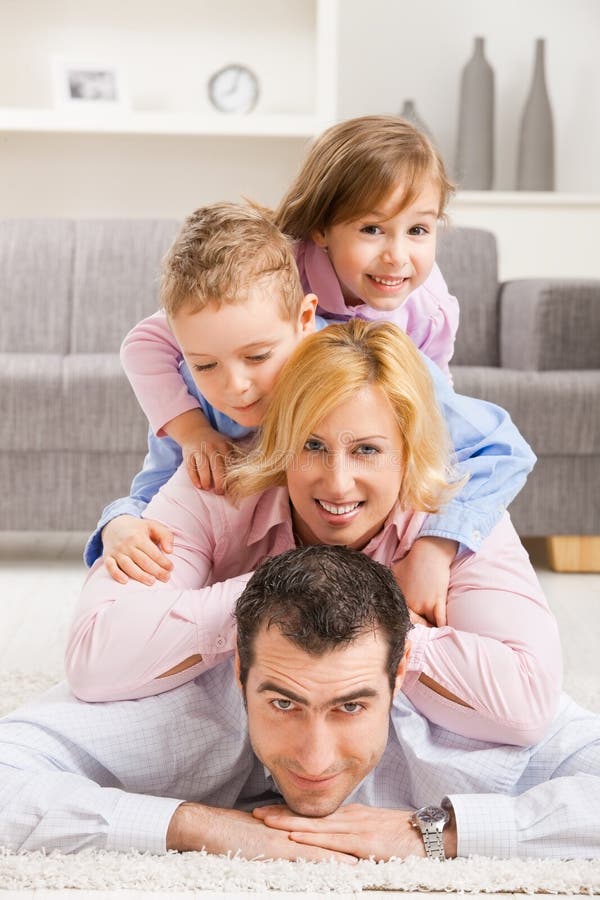 Famiglia felice a casa con la figlia e il figlio, sorridente, disteso ammucchiati sul pavimento nel soggiorno.