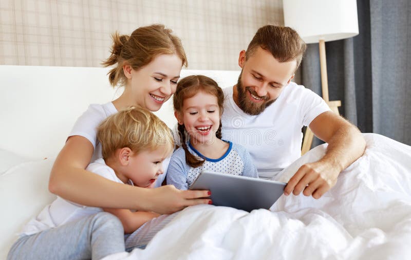 Happy family laughing with tablet computer in bed at home. watching movies and   Internet