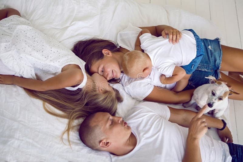Happy family lying on a big white bed in a room stock photo Happy family lying on a big white bed in a room stock photo