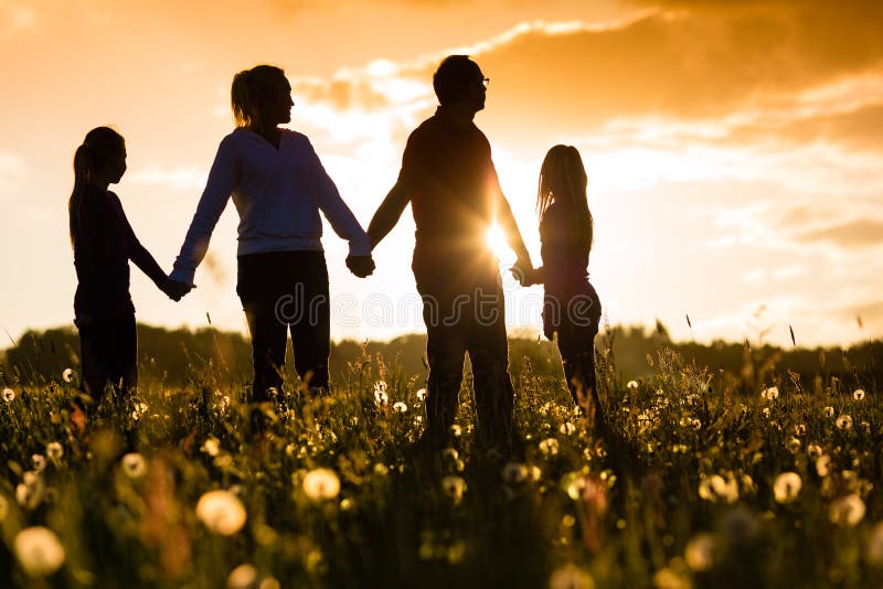 Šťastná rodina s dcerami stála v letní louce při západu slunce.