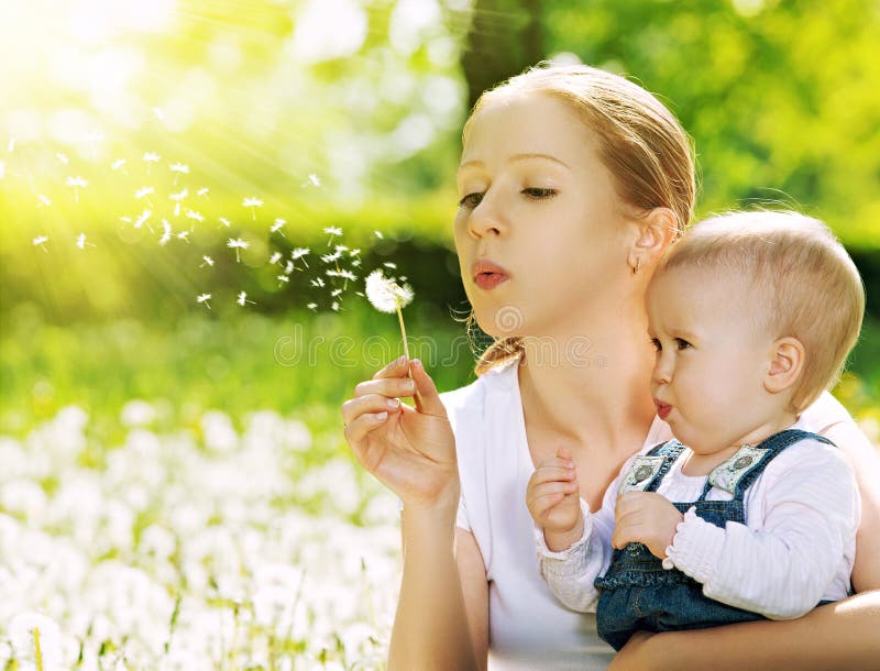 Happy family. Mother and baby girl blowing on a dandelion flower