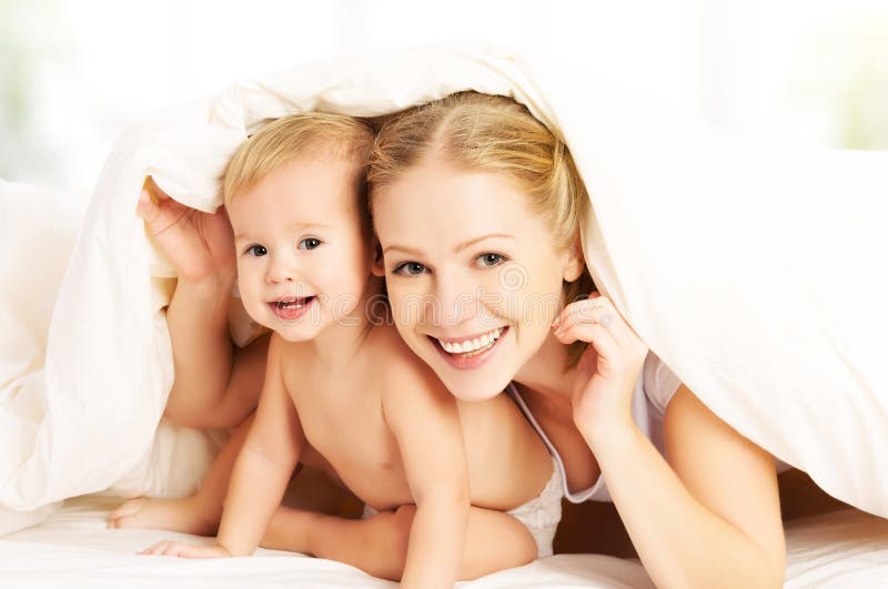 Famiglia felice madre un un bambino sbirciando fuori coperte un letto.