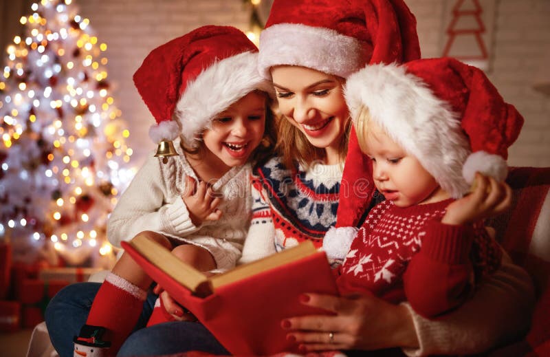 Family mother and children read a book at christmas near firep