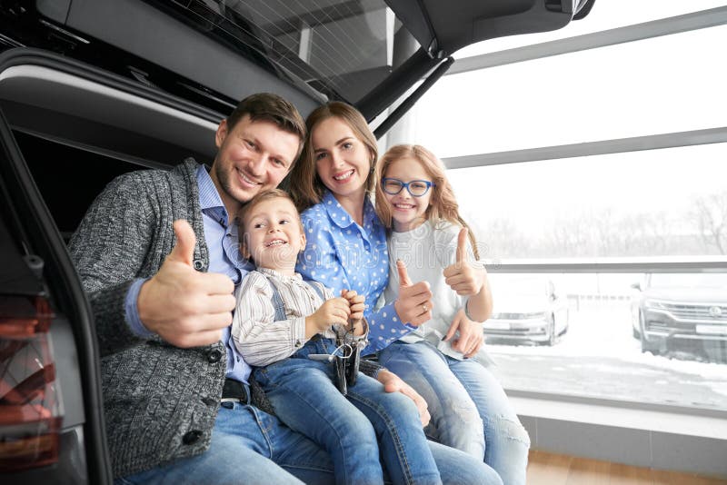 Happy family showing thumbs up, posing in car trunk.